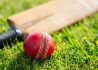 Cricket ball and cricket bat on green grass of cricket pitch